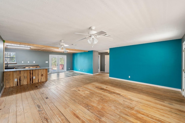 unfurnished living room with ceiling fan, light hardwood / wood-style flooring, a textured ceiling, and french doors