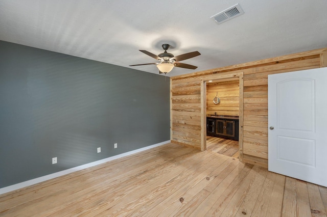 unfurnished living room with wood walls, ceiling fan, and light wood-type flooring