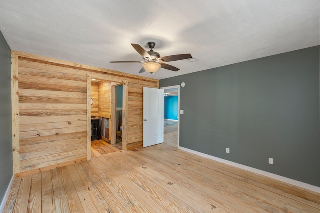 unfurnished bedroom featuring ceiling fan, a textured ceiling, light hardwood / wood-style floors, and wood walls