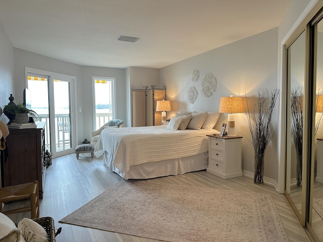 bedroom featuring a barn door, light wood-type flooring, and access to outside