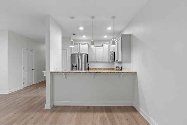 kitchen featuring pendant lighting, appliances with stainless steel finishes, a kitchen bar, and kitchen peninsula