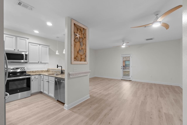 kitchen featuring appliances with stainless steel finishes, decorative light fixtures, sink, white cabinets, and light wood-type flooring