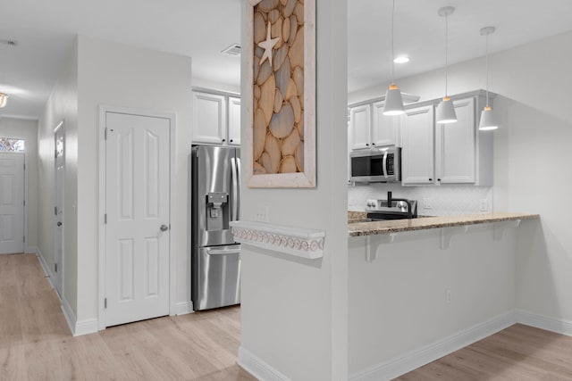 kitchen with appliances with stainless steel finishes, a breakfast bar, white cabinets, hanging light fixtures, and kitchen peninsula