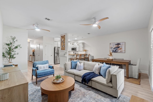 living room featuring baseboards, light wood-type flooring, and ceiling fan