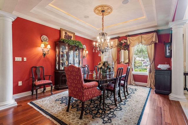 dining area with a raised ceiling, hardwood / wood-style flooring, and ornate columns