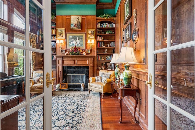 sitting room with hardwood / wood-style floors, a tiled fireplace, built in shelves, and french doors