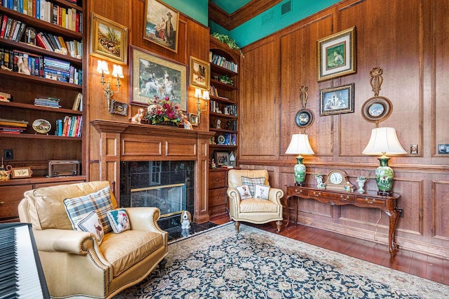 sitting room featuring ornamental molding, wood-type flooring, built in shelves, and a tiled fireplace