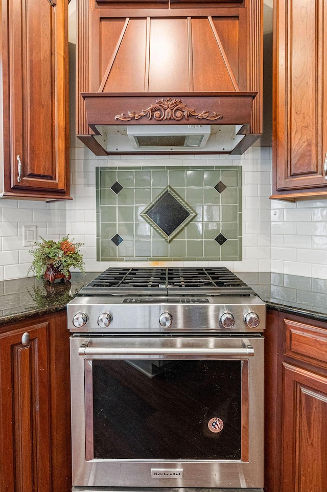 kitchen with dark stone counters, custom range hood, stainless steel range with gas cooktop, and backsplash