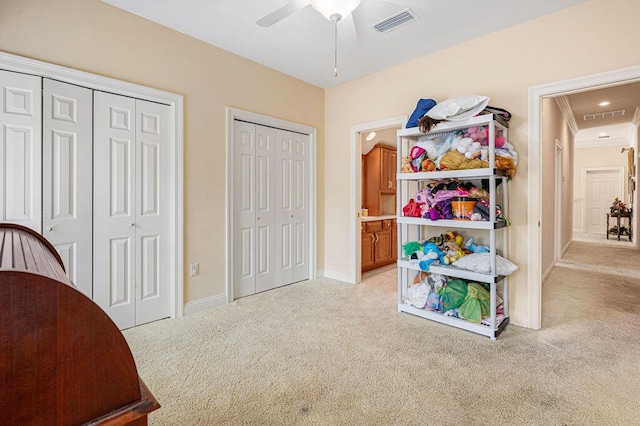 bedroom with ceiling fan, two closets, and light colored carpet