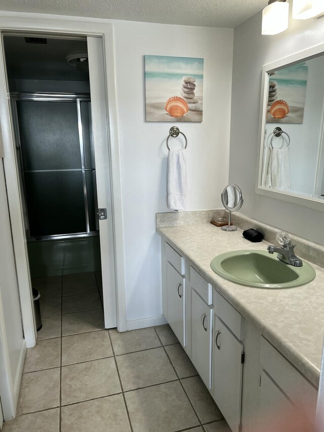 full bath featuring a textured ceiling, a shower stall, tile patterned flooring, baseboards, and vanity