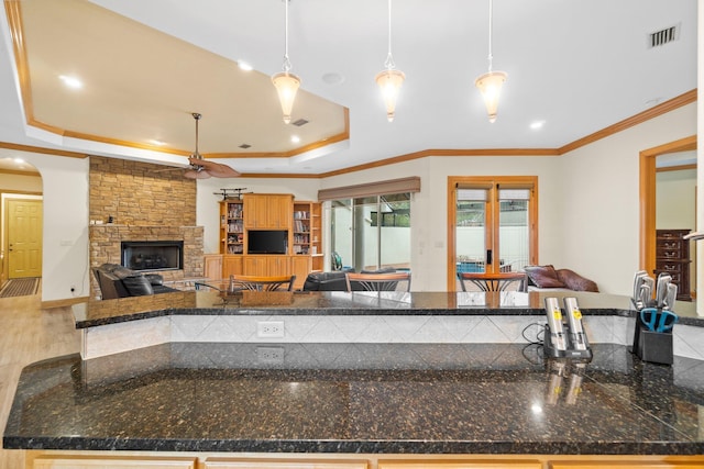 kitchen featuring a fireplace, ornamental molding, a tray ceiling, and hanging light fixtures