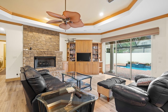 living room with crown molding, light hardwood / wood-style flooring, a raised ceiling, and a stone fireplace