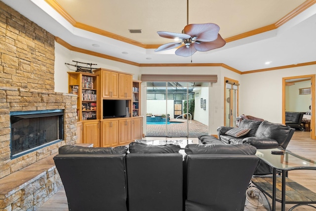 living room with ornamental molding, a tray ceiling, light hardwood / wood-style floors, and a stone fireplace