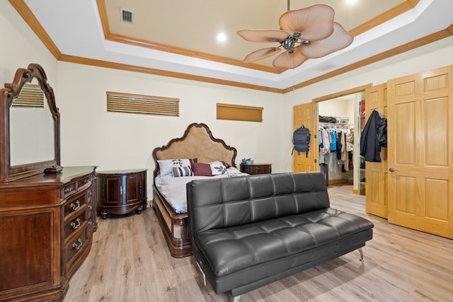 bedroom featuring a tray ceiling, a spacious closet, ornamental molding, and light wood-type flooring