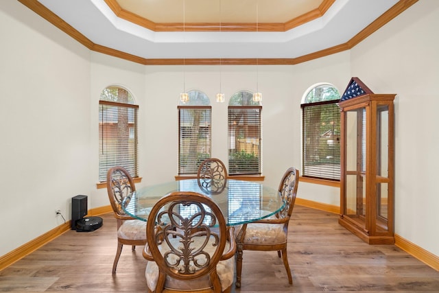 dining space with wood-type flooring, a towering ceiling, crown molding, and a tray ceiling