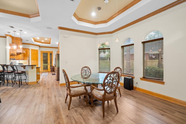 dining room featuring crown molding, a tray ceiling, and light hardwood / wood-style flooring