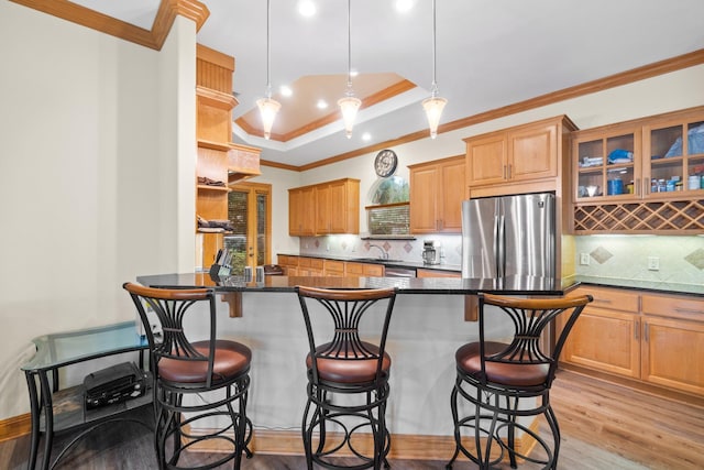 kitchen with a kitchen bar, sink, light wood-type flooring, stainless steel refrigerator, and a raised ceiling