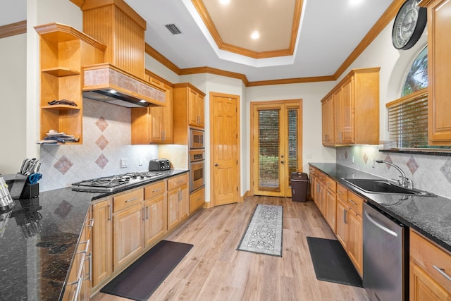 kitchen featuring sink, stainless steel appliances, a tray ceiling, dark stone counters, and light wood-type flooring