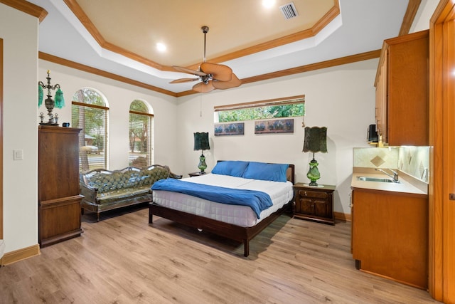 bedroom featuring crown molding, sink, a tray ceiling, and light hardwood / wood-style floors