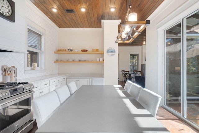 kitchen with stainless steel gas range oven, wood ceiling, white cabinetry, tasteful backsplash, and decorative light fixtures