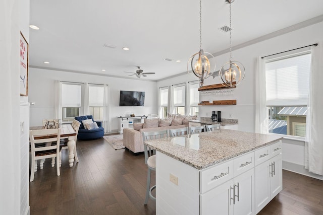 kitchen featuring dark wood-type flooring, white cabinetry, light stone counters, a center island, and hanging light fixtures