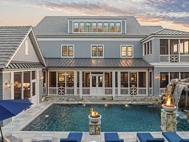 back house at dusk featuring a patio, a sunroom, and a fire pit