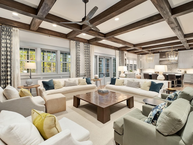 living room featuring coffered ceiling, ceiling fan with notable chandelier, and a healthy amount of sunlight