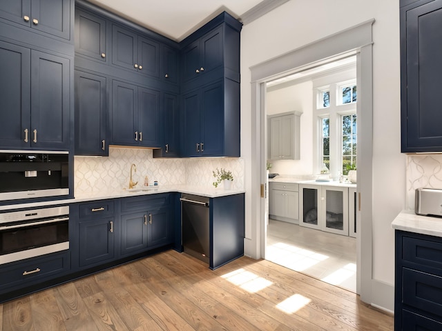 kitchen featuring sink, light hardwood / wood-style flooring, blue cabinetry, tasteful backsplash, and oven