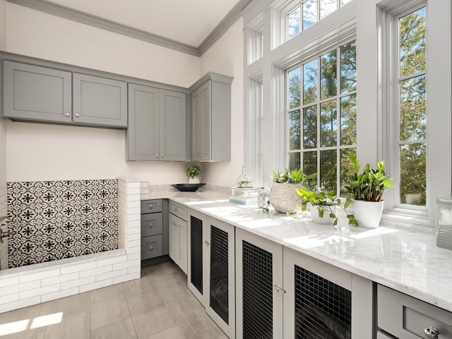 kitchen featuring gray cabinetry, light stone counters, crown molding, and light tile patterned flooring