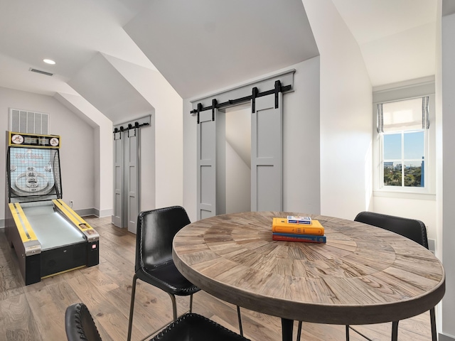 dining space featuring vaulted ceiling, a barn door, and hardwood / wood-style floors