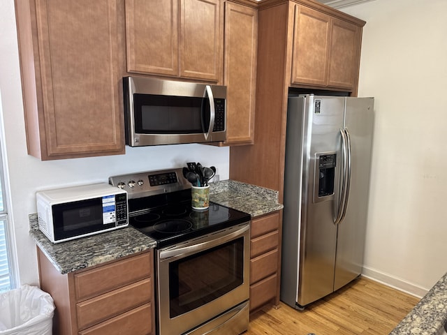 kitchen featuring dark stone countertops, light hardwood / wood-style flooring, and appliances with stainless steel finishes