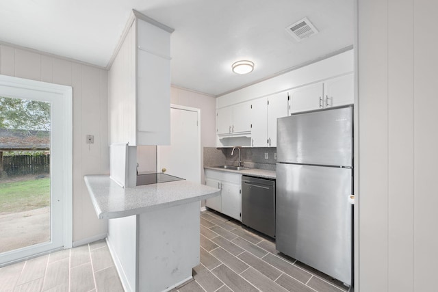 kitchen featuring sink, appliances with stainless steel finishes, white cabinetry, tasteful backsplash, and kitchen peninsula