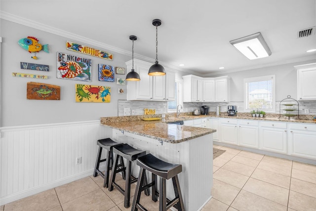 kitchen with visible vents, a wainscoted wall, a peninsula, white cabinetry, and light tile patterned flooring