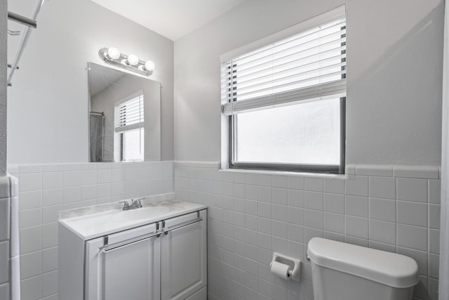 bathroom with plenty of natural light, toilet, vanity, and tile walls