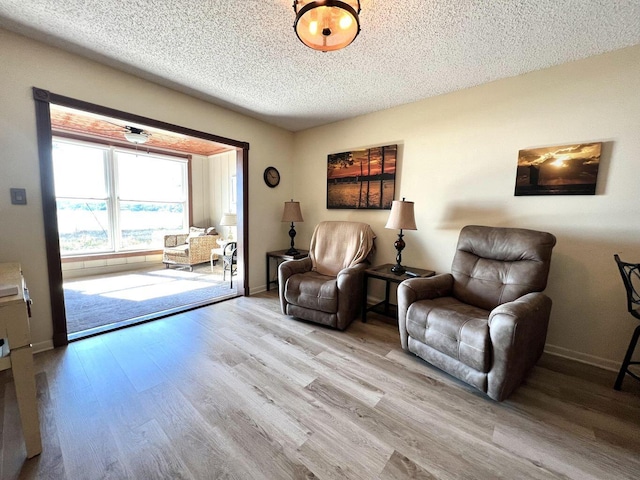 sitting room with light wood-style floors, a textured ceiling, and baseboards