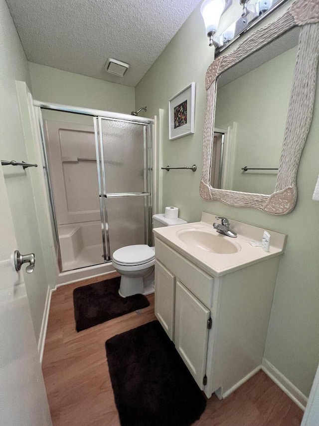 bathroom with a textured ceiling, wood finished floors, toilet, and a shower stall