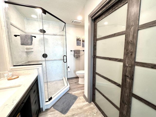 full bath featuring visible vents, toilet, a textured ceiling, a shower stall, and wood finished floors