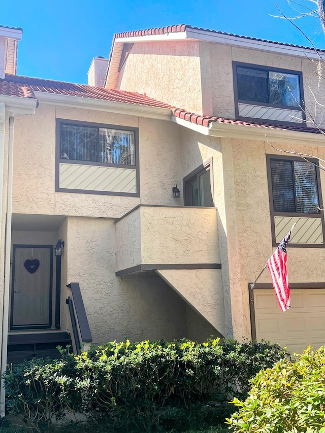 view of side of property featuring a garage, a tiled roof, entry steps, and stucco siding