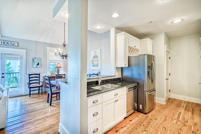 kitchen with appliances with stainless steel finishes, white cabinetry, sink, dark stone countertops, and light wood-type flooring