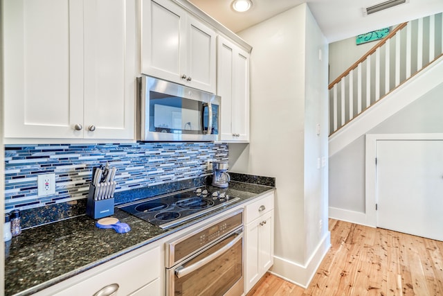 kitchen with white cabinetry, dark stone counters, stainless steel appliances, light hardwood / wood-style floors, and decorative backsplash