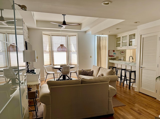 living room featuring ceiling fan, wood-type flooring, and a tray ceiling