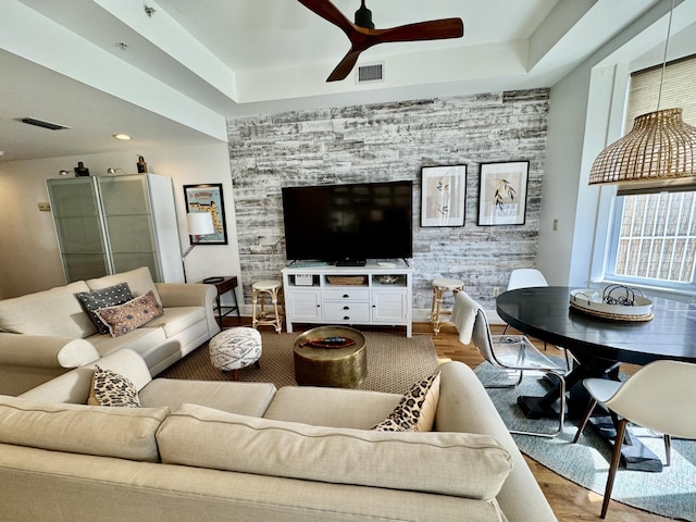 living room with ceiling fan, wood-type flooring, and a tray ceiling