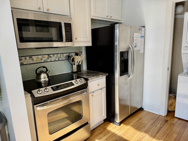 kitchen featuring stacked washer and clothes dryer, white cabinetry, light wood-type flooring, appliances with stainless steel finishes, and backsplash