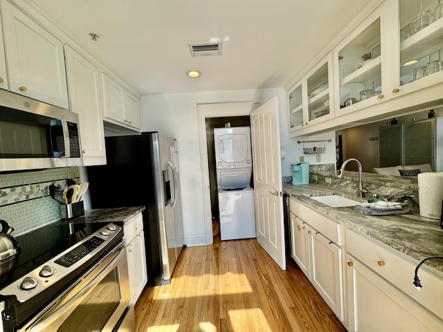 kitchen with sink, stainless steel appliances, stacked washer and clothes dryer, light stone counters, and white cabinets