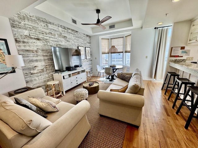 living room featuring light hardwood / wood-style floors, a raised ceiling, and ceiling fan