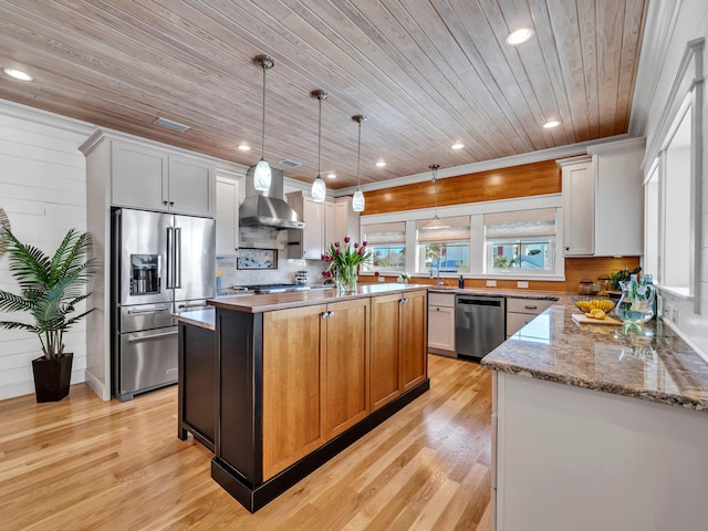 kitchen with wall chimney exhaust hood, white cabinetry, appliances with stainless steel finishes, a kitchen island, and light stone countertops