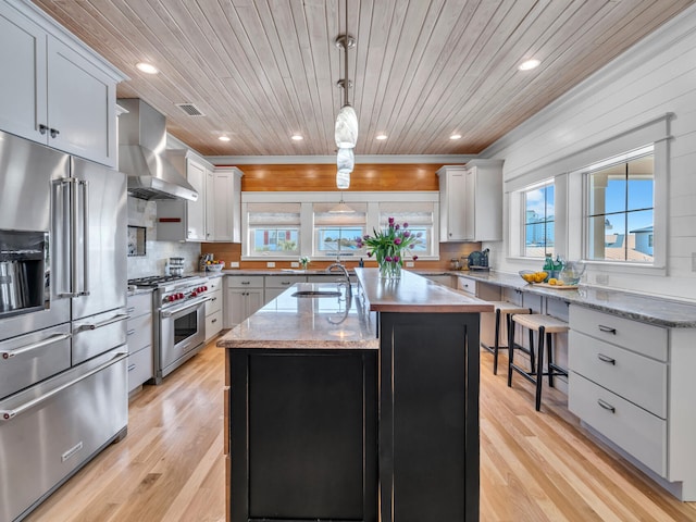 kitchen featuring pendant lighting, sink, high end appliances, a kitchen island with sink, and wall chimney range hood