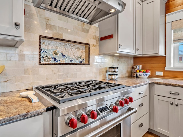 kitchen with wall chimney range hood, white cabinetry, backsplash, light stone counters, and high end stove