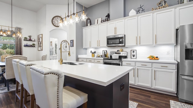 kitchen featuring stainless steel appliances, an island with sink, hanging light fixtures, and white cabinets