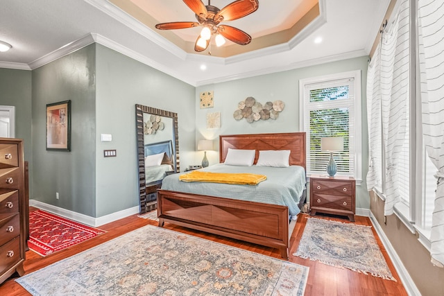 bedroom with a tray ceiling, wood-type flooring, ornamental molding, and ceiling fan